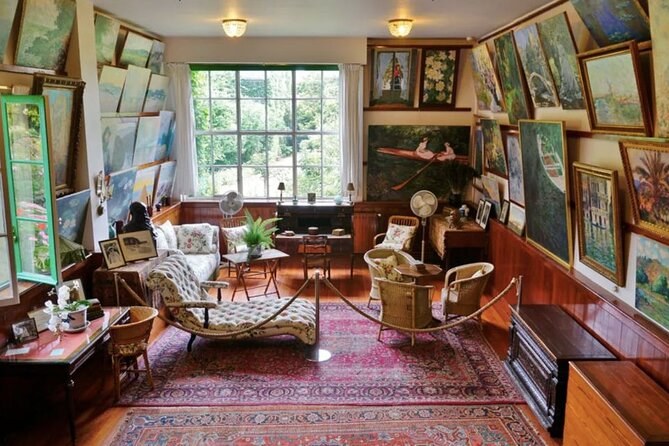 A sitting room hung floor to ceiling with paintings, cane chairs on a patterned rug